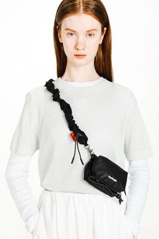Black bungee strap crossbody bag strap with clips; worn over white knit top