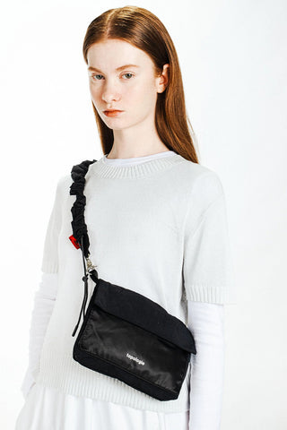 Black bungee strap worn across chest over white sweater with drawcord ends