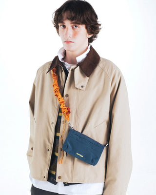 Orange bungee strap detail with metal clips, worn across chest on a messenger bag
