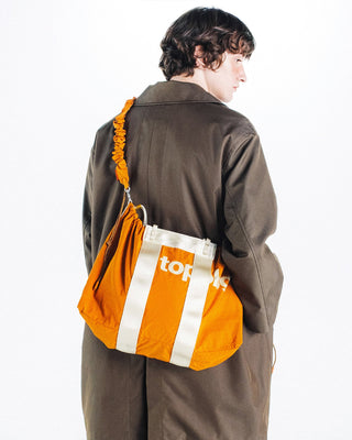 Orange bungee strap crossbody with ruched elastic and clips on an orange-and-white bag