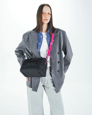Pink bungee strap with clip hardware across the chest on a dark crossbody bag