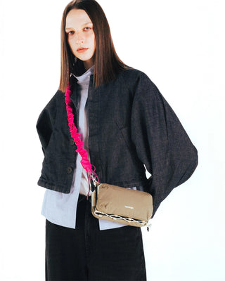 Pink bungee strap with carabiner clips over shoulder on a tan crossbody bag