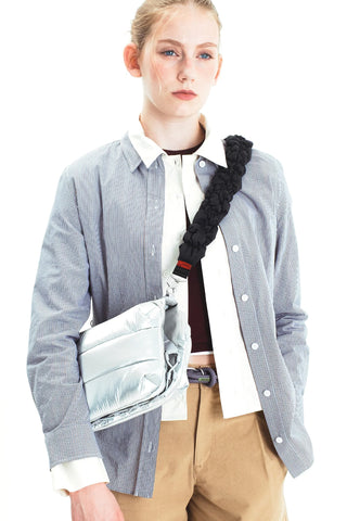 Braided dark crossbody strap with metal clips worn over a light shirt