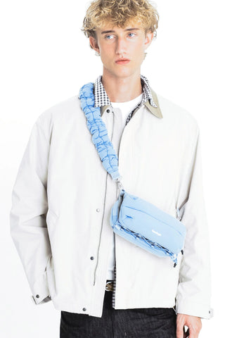 Light blue ruffled crossbody strap with pouch and metal buckles, worn on torso