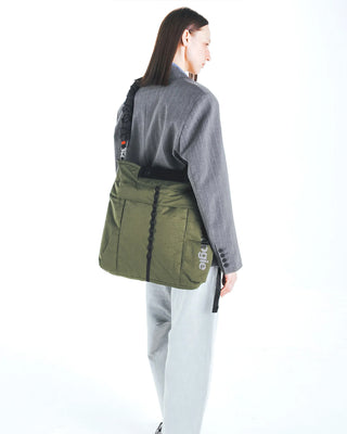 Deep green nylon helmet bag worn at side, blue logo patch on front panel