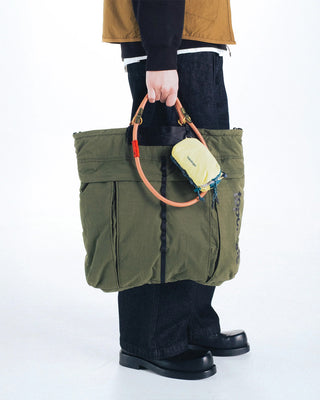 Deep green nylon helmet bag held by orange handle strap with padded front