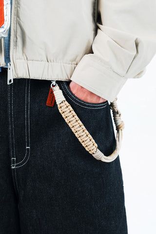 Braided macrame wrist strap in tan with metal clips and red tag, shown close-up