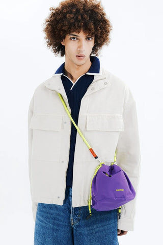 Purple reversible bucket bag with drawstring and topologie logo, worn with neon strap.
