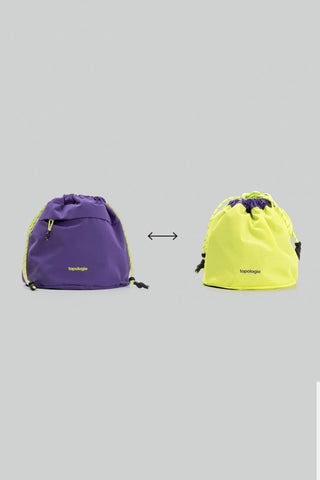 Reversible bucket bag shown in purple and neon yellow with drawstrings and cord ties.