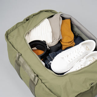 Olive duffle bag open showing white sneakers and packed items inside