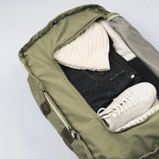 Olive duffle bag open with light interior lining and white sneakers inside