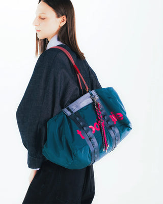 Deep teal duffle bag worn crossbody with red zipper pulls and logo print