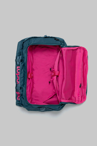 Small duffel bag open to reveal bright pink interior lining and zippered pocket, teal exterior