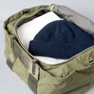Open moss green duffle bag holding folded dark blue knit fabric