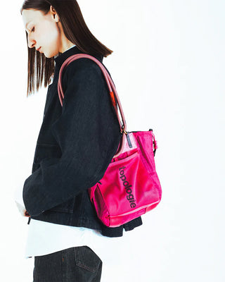 Small pink tote bag with drawstring cords, worn by a model; “topologie” print