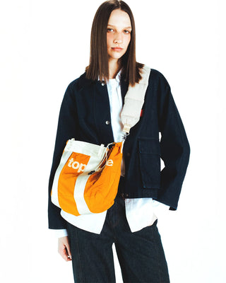 Topologie small tote on model, burn orange with white stripes and drawstring closure.