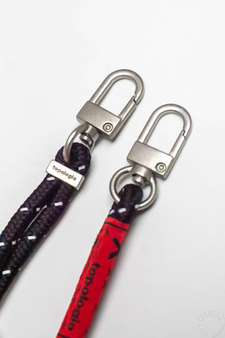 Topologie 6mm rope strap close-up: black rope, red label, silver carabiner clips