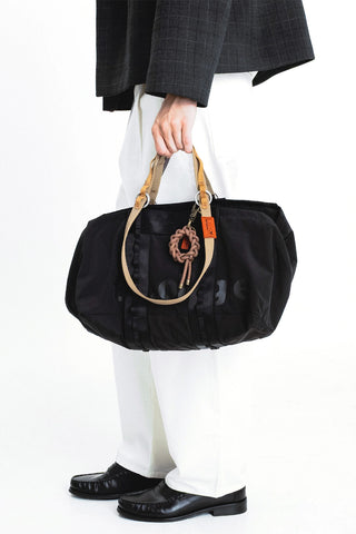 Brown rope keychain charm on a black duffel-style bag with tan handle