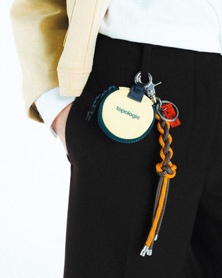 Keychain charm with circular tag and orange braided cord attached to pants