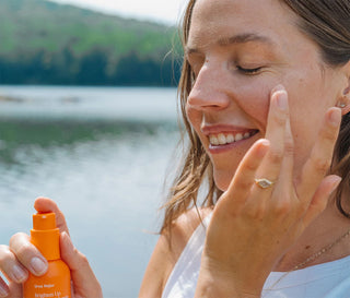Woman applying orange vitamin C serum to face with pump bottle nearby