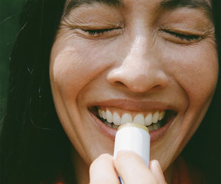 Woman smiling while applying a white lip balm stick to her lips