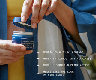 Hands holding a blue recovery cream jar during skincare application.