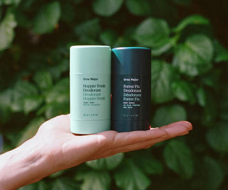 Two deodorant sticks, mint teal and dark blue, held in a hand.