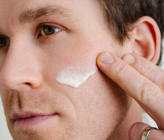 Man applying white skincare serum to cheek with fingertips