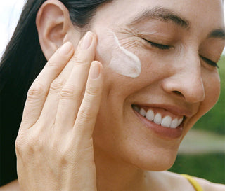 Woman smiling while smoothing white serum on cheek near eyes
