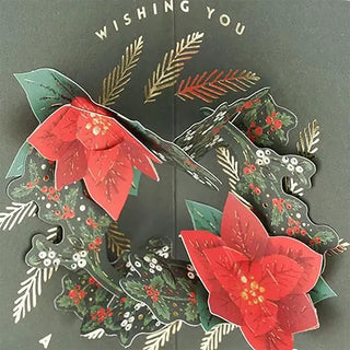 Close-up pop-up poinsettia wreath on green Christmas card with red flowers and greenery