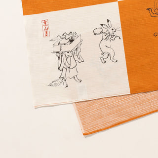 Orange and white furoshiki with square panels and black line animal/figure art