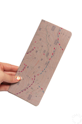 Hand holding weather map notebook, beige cover with red and blue route markings