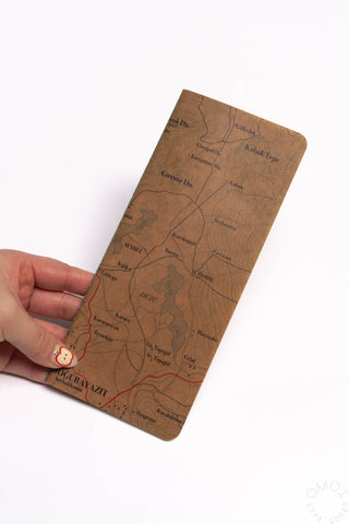 Hand holding topographical map notebook with brown illustrated cover