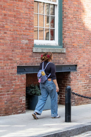 Person wearing a lilac mini backpack with shoulder strap on a city sidewalk