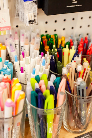 An extreme close up shot of the colorful pens and markers on the sales floor. Each brand separated in different cups.