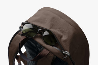 Brown daypack with sunglasses tucked into the front mesh pocket