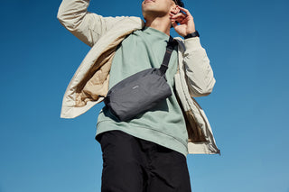 Dark gray crossbody sling bag worn diagonally on a person outdoors.