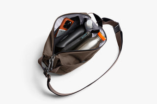 Brown sling bag open to show interior compartments and zip closure.