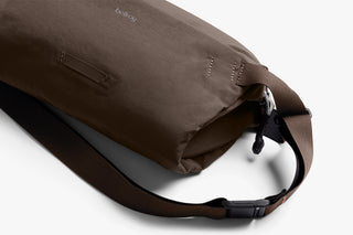 Brown sling bag with side zipper, pull tab, and adjustable shoulder strap.