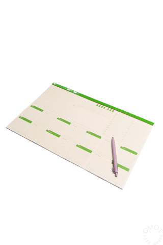 Two-week desk planner with green day blocks and purple pen resting on it