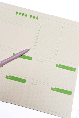 Two-week desk planner close-up with green blocks and purple pen