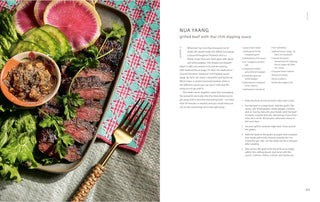 Cookbook open spread with serving tray of grilled meat and fresh greens