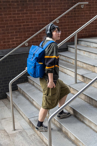 Indigo rolltop backpack worn by a person, blue bag with orange strap details