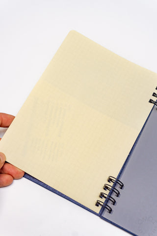 Hand holding open navy spiral notebook with cream refill pages