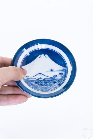 Blue mini ceramic plate held in hand, white rim with mountain scene and plants