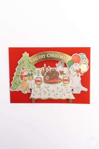 Pop-up Christmas card with cats around a table and “Merry Christmas” on red cover