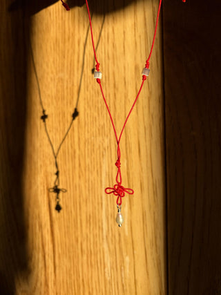 Lucky knot necklace with red cord, clover pendant, and small pearl drop