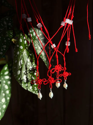 Lucky knot necklace display of red cords with clover knots and pearl tassel beads