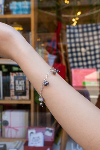 Silver-tone bracelet on wrist with dangling green and pearl beads and dark accents