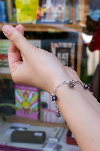 Silver-tone bracelet with dark bead charms and small dangling loops on wrist